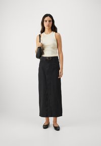 Falda maxi de mezclilla negra con una costura frontal, cintura con cinturón, combinada con una camiseta ajustada color crema y zapatos planos negros, llevada con un pequeño bolso negro.