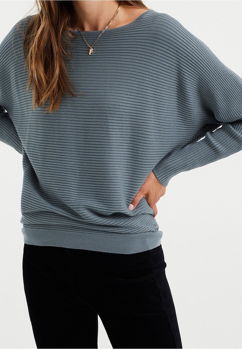 Jasnoniebieski ribbed sweter o luźnym kroju, szerokim dekolcie i długich rękawach, zestawiony z czarnymi spodniami z kordurowej tkaniny. Gładka tekstura, casualowy design.