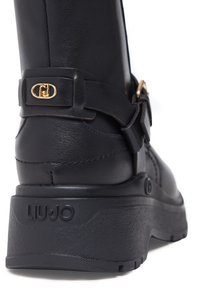 Schwarzer Leder-Stiefelette mit dekorativer goldener Schnalle, strukturierter Sohle und geprägtem "LIU.JO"-Logo an der Ferse. Abgerundetes Zehendesign.