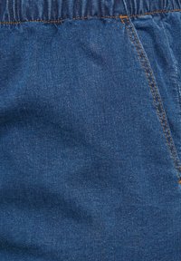 Tela de mezclilla en azul profundo, cuenta con una cintura elástica y costuras visibles en un tono más claro. Textura suave con ligero brillo.