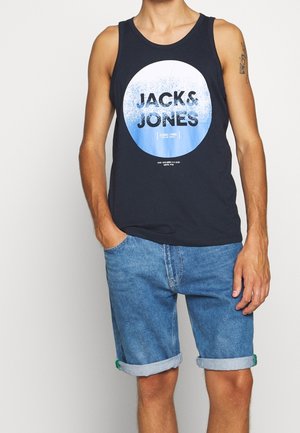 Débardeur bleu marine avec un graphisme circulaire portant l'inscription "JACK & JONES" et un accent dégradé bleu, associé à un short en jean retroussé avec un ourlet effiloché.