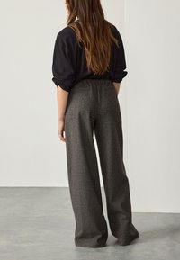 Wide-leg trousers in a textured gray fabric, featuring a high waistband and subtle checks, with a classic back pocket detail.