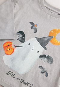 Szara koszula z długim rękawem z nadrukiem ducha oraz nietoperzy i dyni, z akcentami w kolorze pomarańczowym i czarnym, oraz napisem "Cukierek albo psikus?".