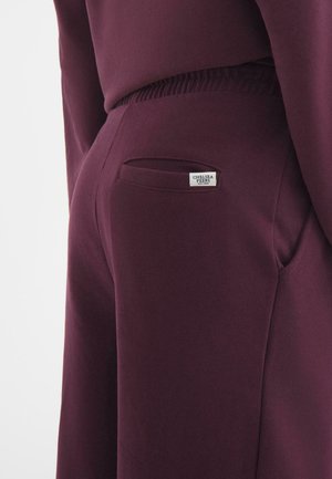 Jogger bordeaux realizzati in tessuto morbido, con una tasca laterale e una piccola etichetta con "Chelsea Peers" sul retro.