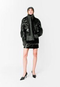 Chaqueta bomber de cuero negra sobre una bufanda de punto gris, minifalda negra con detalles metálicos y tacones altos negros con adornos.