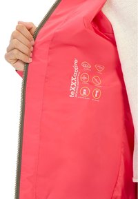 Bright pink jacket interior featuring a smooth texture with a branded tag. Icons indicate waterproof, windproof, and sealed seams features.
