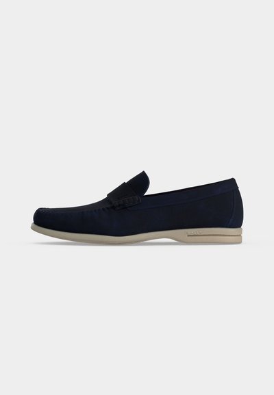 Mocassin homme en daim bleu marine avec semelle en caoutchouc beige clair et une sangle décorative sur la partie supérieure.