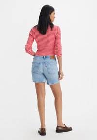 Röd och vit randig långärmad topp i kombination med ljusblå denimshorts. Påfallande sömmar på bakfickorna och detaljer med brunt lädermärke.