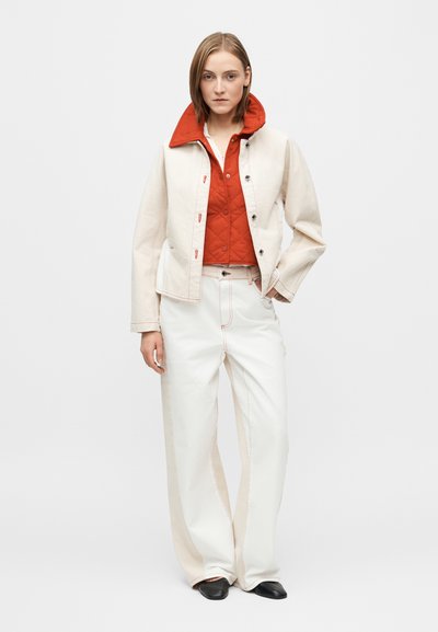 Μπεζ τζιν μπουφάν με κόκκινο γιακά, συνοδευόμενο από κόκκινο επενδεδυμένο εσωτερικό στρώμα και λευκό παντελόνι με φαρδιά μπατζάκια και αντίθετες ραφές. Μαύρα παπούτσια.