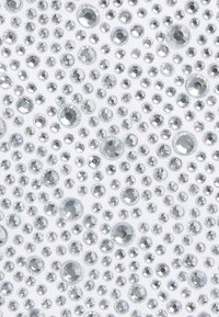 Embellishments de cristal dispuestas en diferentes tamaños sobre un fondo de tela blanca. La superficie tiene una textura brillante con cualidades reflectantes.