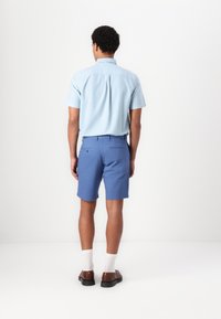 Chemise bleu clair à manches courtes, coupe ajustée, assortie à un short bleu. Complété par des chaussures marron et des chaussettes blanches. Design simple, sans motifs visibles.