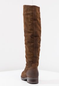Botte haute en daim marron avec une surface texturée, bout rond et talon empilé. Présente une couture le long de l'arrière pour un détail supplémentaire.