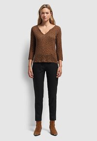 Brown leopard print top with a V-neck and three-quarter sleeves, paired with black pants and tan ankle boots with metallic accents.