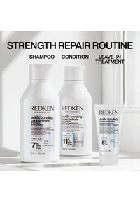 Trzy produkty do pielęgnacji włosów marki Redken z etykietami: acidic bonding concentrate szampon, odżywka oraz kuracja bez spłukiwania, na białej powierzchni blisko okna.