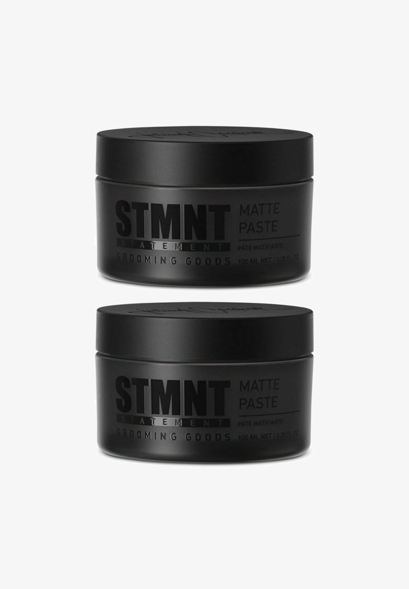 Two black, matte jars of STMTNT Matte Paste, each 100 ml, labeled clearly with product and brand information in bold gray text.