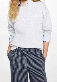 Světlé šedé mikina s potiskem a grafikou tenisu, spárovaná s kalhotami v námořnické a bílé barvě s pruhy, volným střihem a kapsami.