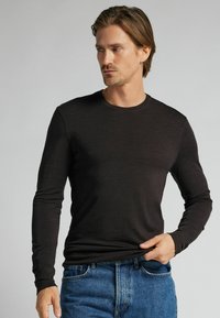 Langärmliges schwarzes Shirt aus einem weichen, strukturierten Stoff. Verfügt über einen runden Halsausschnitt und angepasste Ärmel, kombiniert mit blauen Jeans.