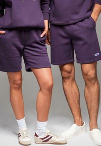 Fialové šortky z bavlněné směsi s elastickým pasem a bočními kapsami, v kombinaci se světlými teniskami. Design má úhledný, strukturovaný střih.
