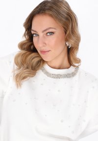 Felpa bianca con decorazioni in perle e scollo arricchito da diamanti, caratterizzata da una texture liscia e una vestibilità comoda.