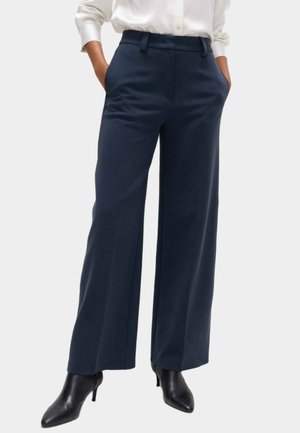 Pantaloni a gamba larga navy in tessuto leggero, con vita sartoriale, tasche laterali e una texture liscia. Abbinati a scarpe nere con tacco.
