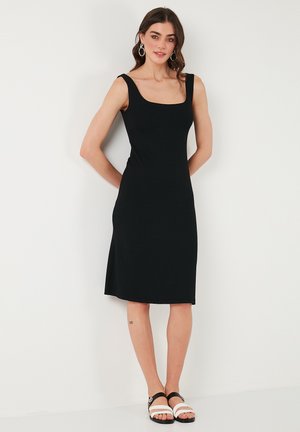 Black ribbed midi dress with wide shoulder straps, relaxed fit, and a scooped neckline. Styled with black and white sandals.