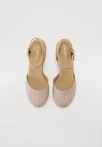 Beige slingback sko med en tekstureret stofoverdel, elastisk rem og en lille gul accent på siden. Flad sål og rund tå design.