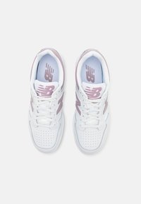 Vitaidro skor i vitt med ljusrosa detaljer, perforerad tåbox, platta snören och en vadderad innersula med New Balance-logotyp.