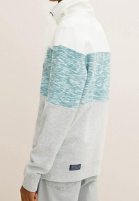 Pullover grigio chiaro con pannello superiore texturizzato turchese e colletto bianco. Presenta polsini a coste e un'etichetta del marchio blu navy sull'orlo.