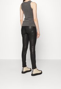 Top senza maniche grigio abbinato a pantaloni skinny in pelle nera e stivaletti fino alla caviglia crema con accenti neri e design con lacci.