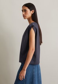 Dark gray, short-sleeve top in soft fabric, features a relaxed fit with subtle pleats at the shoulder. Paired with a denim skirt.