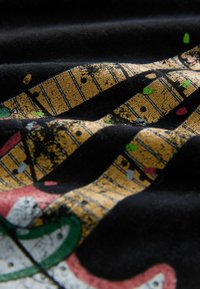 Czarna tkanina z motywem graficznym w kolorze złotym, zawierająca elementy muzyczne oraz kolorowe akcenty w czerwieni, zieleni i niebieskim. Widoczna fakturowana powierzchnia.