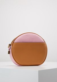 Okrągła torebka z brązowym, teksturowanym spodem z skóry oraz gładkim różowym wierzchem, wyposażona w złoty zamek błyskawiczny i boczny pasek.