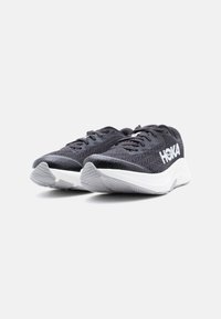 Ζευγάρι μαύρα αθλητικά παπούτσια Hoka με λευκές μεσαίες σόλες, πλεκτά επάνω μέρη και γκρι σόλες με σχεδιασμό πάτου, σε λευκό φόντο.