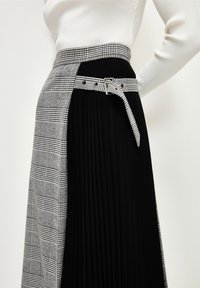 Woman wearing a high-waisted skirt with black pleats and black-and-white checkered fabric details, paired with a matching checkered belt.