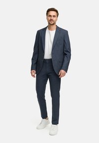 Marineblauw gestructureerd pak met een getailleerd jasje en slim-fit broek, gecombineerd met een wit t-shirt en witte sneakers.