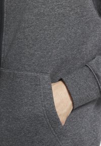 Charcoal gray zip-up hoodie, cotton blend, featuring a front pocket, ribbed cuffs, and a textured fabric finish.