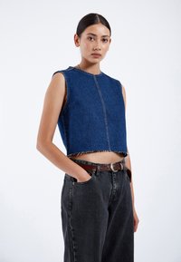 Top corto de mezclilla con escote redondo, dobladillo deshilachado y diseño sin mangas. Combinado con jeans de tiro alto en gris oscuro y un cinturón marrón.