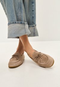 Beige ruskinds loafers med snøring, rund tå og en fleksibel sål, parret med cropped lyseblå denimbukser.