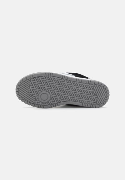 Zapatilla en blanco y negro con una suela de goma gris texturizada, que presenta un dibujo en el diseño de la suela y un acento circular en el talón.