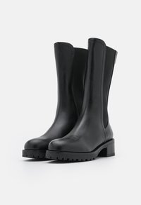 Botines de cuero negro con un acabado suave, paneles laterales elásticos y un tacón bajo en bloque. Presentan una suela de goma con relieve para mayor agarre.