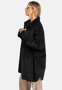 Schwarze Cordjacke mit Kragen, knöpfbarem Vorderteil und Seitentaschen. Sie hat eine vertikale Rippstruktur und einen lässigen Schnitt.