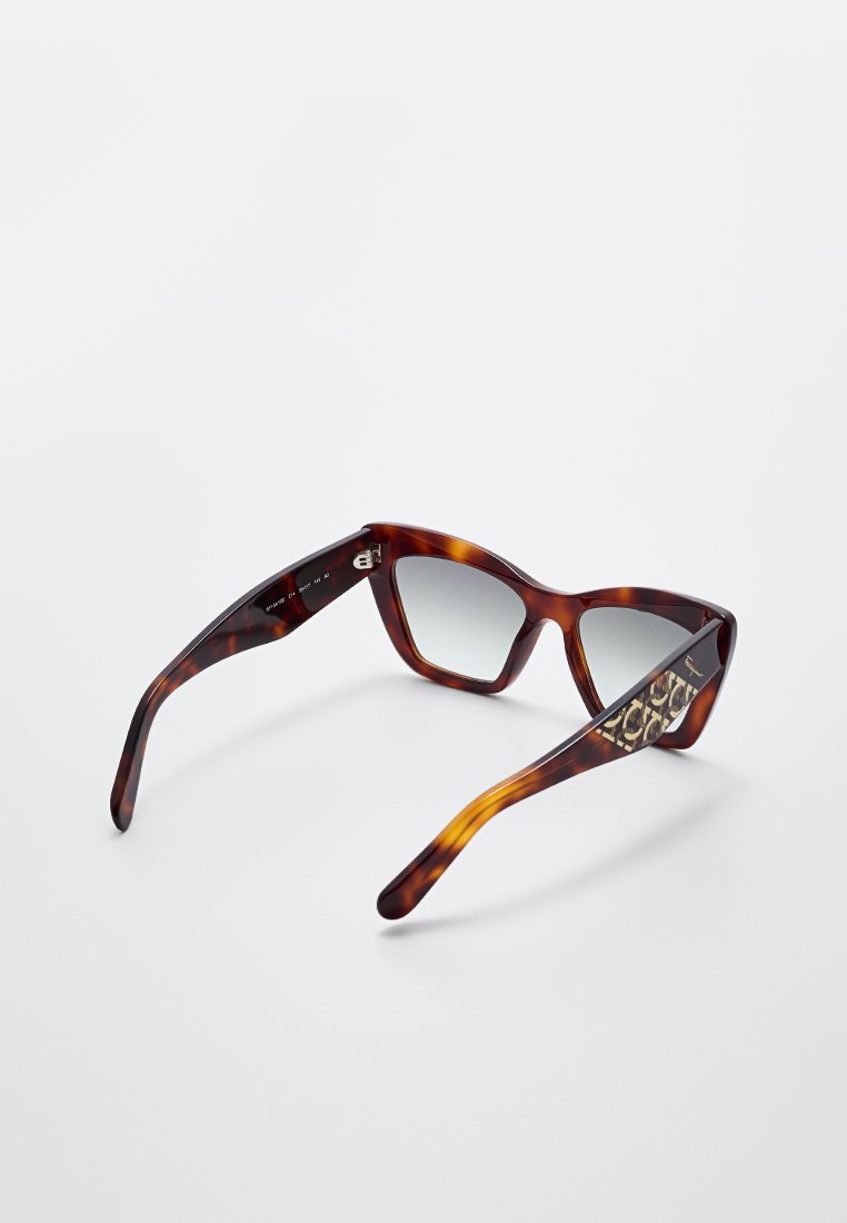Gafas de sol de ojos de gato en carey marrón con lentes grises. Las patillas presentan un distintivo acento con un patrón, añadiendo un detalle al diseño.