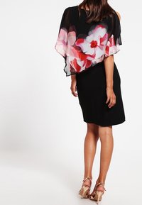 Schwarzes Kleid mit einem durchsichtigen floralen Überzug in Rosa- und Rottönen; knielang; weicher Stoff mit fließenden, kapuzenartigen Ärmeln; Riemchen-Heels.