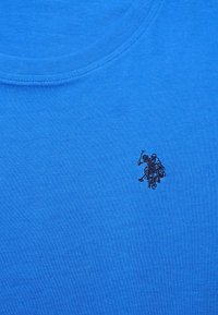 Modré bavlněné tričko s kulatým výstřihem, které na levé straně hrudi zdobí malé černé vyšívané logo jezdeckého postavy.