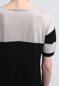 Haut noir et argent à manches courtes avec un motif à rayures horizontales ; texture lisse, encolure ronde et manches contrastantes.