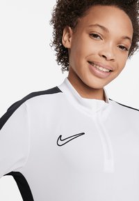Top atlético blanco con detalles negros, diseño de medio zip y logo de Nike en el pecho. Fabricado con una tela suave, presenta una silueta ajustada.