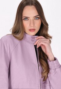 Lavendel leren jas met een hoge kraag, een ritssluiting aan de voorkant en twee knopen als accent. Beschikt over een gestructureerde afwerking en verzamelde manchetten.