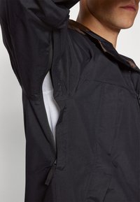 Chaqueta negra con cierre de cremallera y forro en contraste. Textura suave con un diseño estructurado y costuras anguladas.