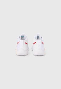Witte sportschoenen met rode accenten, gestructureerde zijkanten, achterste trekkkoorden en een gewatteerde zool. Contrasterende lichtere zoolkleur.