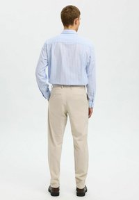 Camisa de botón a rayas azul claro con mangas largas, combinada con pantalones beige. La vista trasera muestra dos bolsillos en la parte posterior y un ajuste relajado.